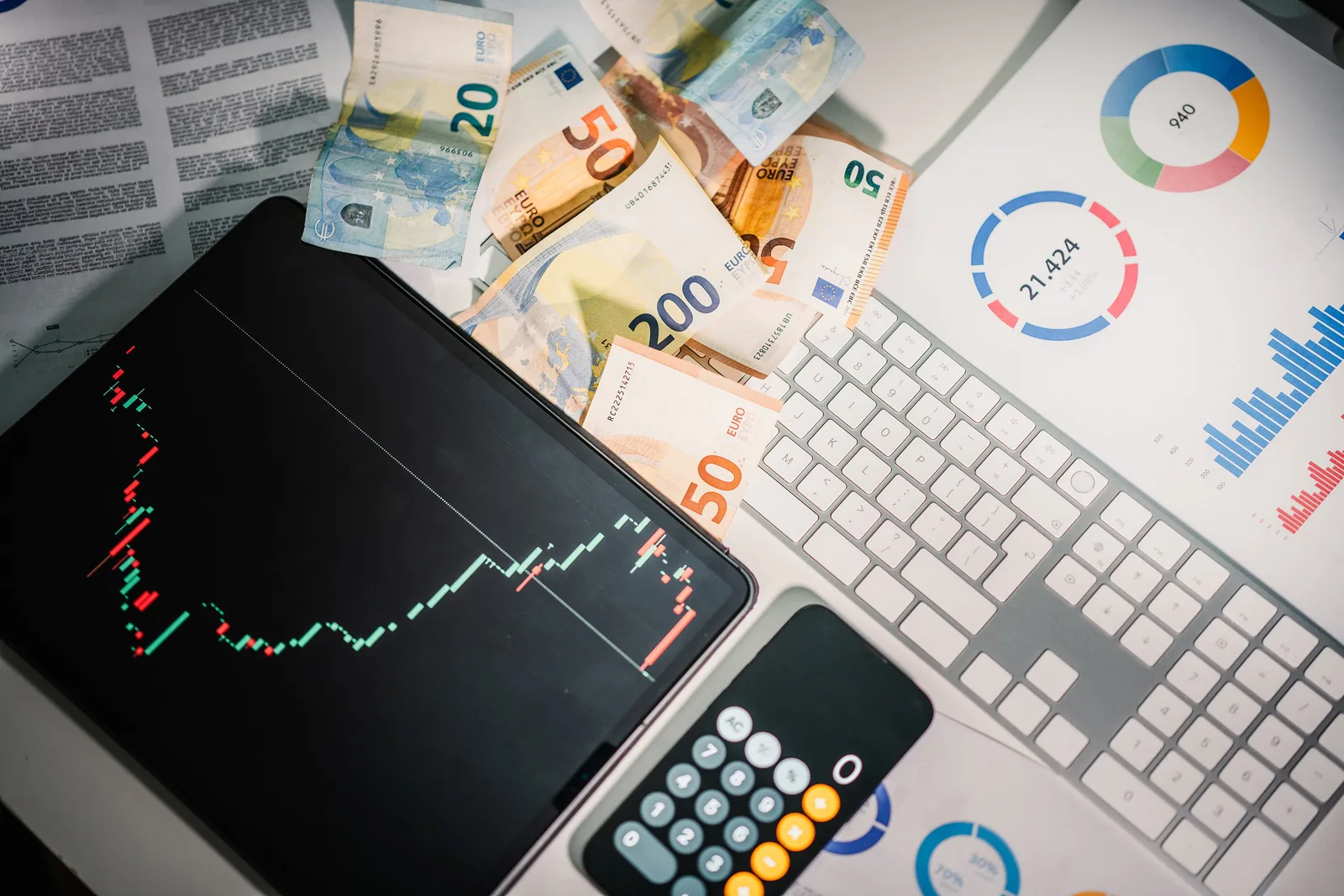 Overhead view of financial tools with Euro banknotes on a desk showing market trends and graphs.
