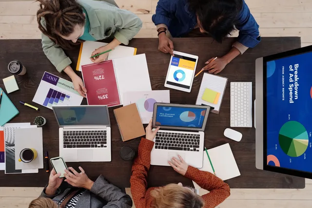A diverse team collaborating on digital marketing strategies at a desk, using laptops and tablets. Awin vs Tradedoubler: how to compare UK network quotes
